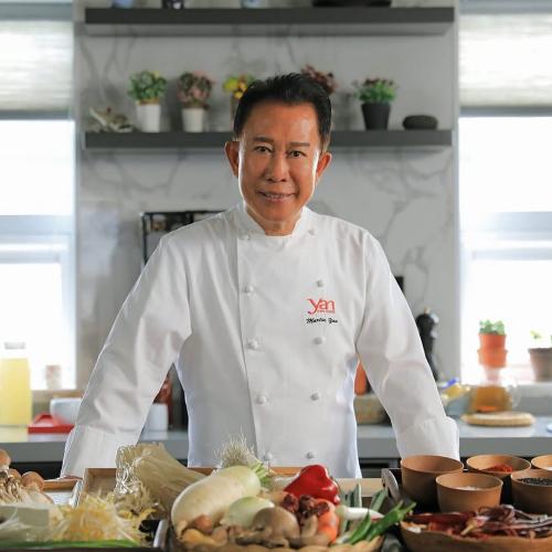 A chef stands in a kitchen, in front of him many ingredients.