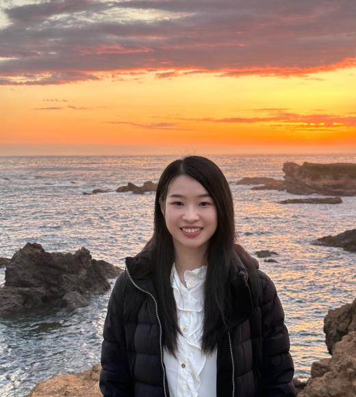 Li Liao smiles while the sun sets over the ocean behind her.