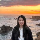 Li Zhi Liao stands in front of the ocean at sunset.
